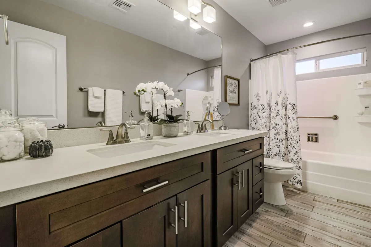 A spacious, modern bathroom featuring double vanity sinks, elegant lighting fixtures, and decorative plants. The tranquil setting is perfect for morning routines or relaxing evening rituals, and the layout highlights both luxury and functionality.