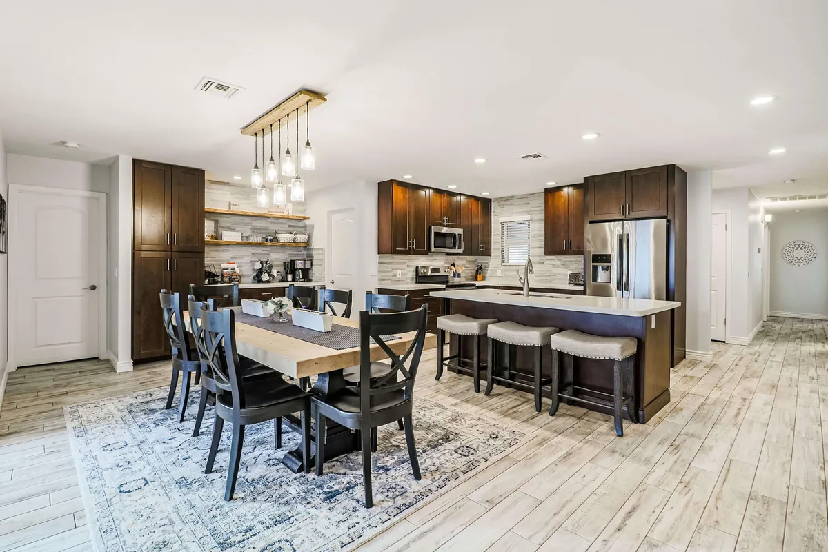 This interior shot centers on a generous dining table set for multiple guests, a kitchen island with barstools, stylish pendant lighting, and modern wood cabinetry. The seamless flow between kitchen and dining area encourages shared meals and lively conversation.