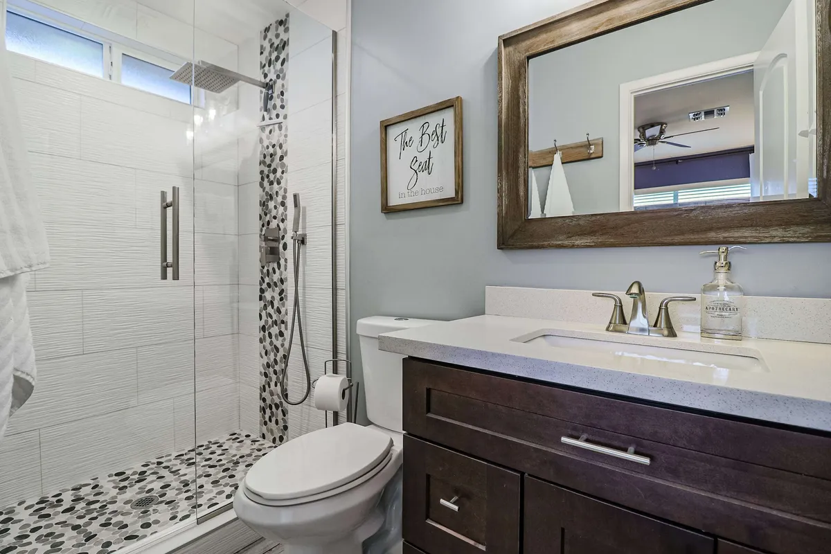 A bright, calming bathroom featuring a spacious shower area, modern vanity, large mirror, and a decorative sign. The ambiance suggests a refreshing environment for self-care and rejuvenation.