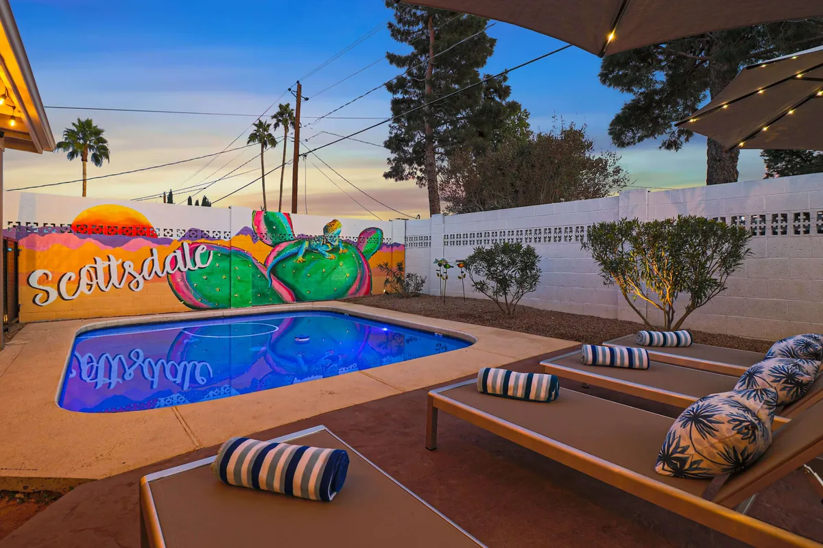 A vibrant pool area highlighted by a striking cactus mural, surrounded by lounge chairs and palm trees. The scene evokes a sense of fun and relaxation, with ample space for swimming, sunbathing, and evening cocktail parties.