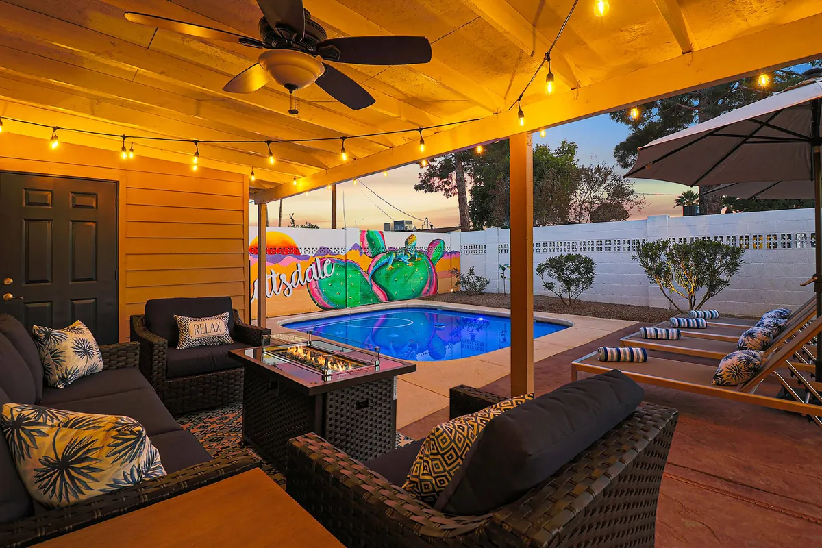 The image showcases a vibrant Scottsdale backyard featuring a sparkling swimming pool, inviting outdoor seating area, a bold and colorful mural, and a cozy fire pit. String lights set a festive mood, highlighting the perfect space for both lively gatherings and peaceful relaxation.