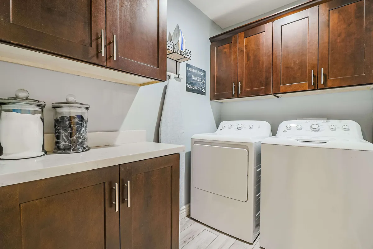 This image features a practical and tidy laundry area equipped with a modern washer and dryer, ample cabinetry for storage, stylish glass jars, and a decorative sign adding a welcoming touch. The space exudes efficiency and family functionality, emphasizing the home's readiness to accommodate the practical needs of families during their stay.