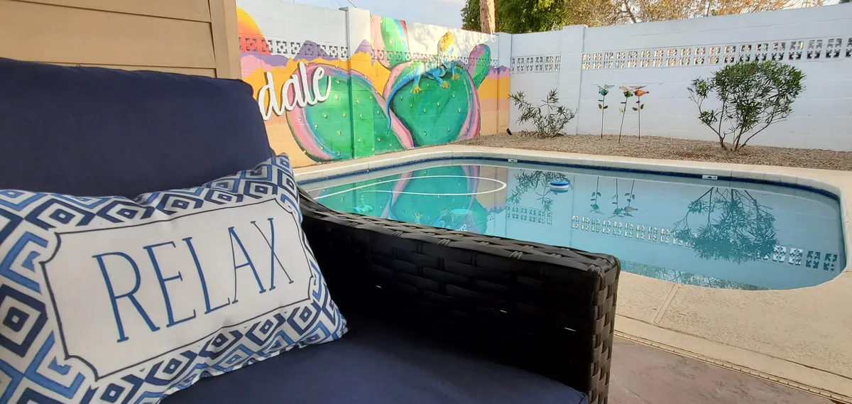 This image showcases a sparkling outdoor pool with a colorful mural as a backdrop and a lounge chair topped with a 'RELAX' pillow. The scene is inviting, with space for swimming, sunbathing, and socializing, all set in a serene environment perfect for unwinding after a day of adventure.