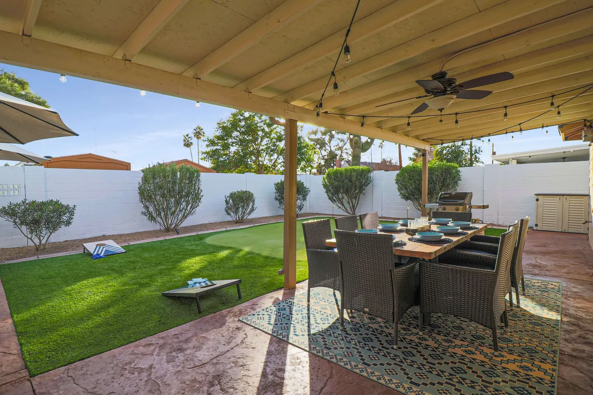An outdoor dining table sits on a green lawn beneath glowing string lights, set for al fresco meals or festive gatherings. The surrounding landscaping creates a cheerful, private outdoor dining experience under the Arizona sky.